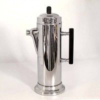 Front side view of the chrome cocktail shaker showing its height, spout, and bakelite handle.