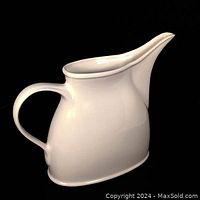 Front side view of white ceramic pitcher showing smooth curved handle and elongated spout