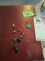 Photo showing all earrings and pendant on a red surface, including turquoise bead drop earrings, pendant, and 4 pairs of stud earrings.