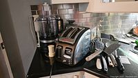KitchenAid food processor with lid and bowl, T-Fal 2-slice toaster, utensils including spatulas and slotted spoon on countertop.