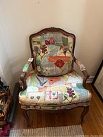 Front view of the upholstered Bergere style armchair with multicolored floral and abstract pattern upholstery and matching pillow.