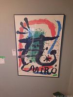Photo of framed Joan Miró print hanging on wall showing colorful abstract print and signature.