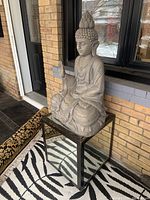 Front angle of resin Buddha figure sitting on mirrored composite wood table with wheels, showing the overall condition and design.