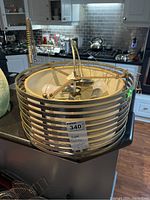 Photo of a round ceiling light fixture with horizontal metal stripes and three bulb sockets inside, placed on a kitchen counter.