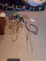Photo showing assorted costume jewelry including necklaces, bracelets, earrings, rings, and a pewter letter opener laid out on a surface.