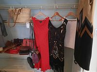 Three women's dresses hanging on heart-shaped hangers, a tan woven tote handbag on shelf above, multiple handbags on shelf below.