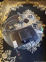 Panasonic DVD home theater system main unit with remote, cables, and Apple TV device on glass table on patterned rug.