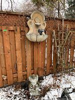 Mounted garden fountain hanging on wooden fence outdoors with solar light and vegetation around.