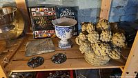 Shelf with gardening books, ceramic urn vase, resin garden step stone, stained glass coasters, and resin artichoke sculpture