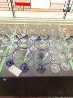 Top view of assorted glassware including martini glasses with blue rims and stems, clear wine glasses, and other glasses on a table.