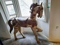 Wooden horse statue in front of window, showing full side profile and decorative saddle.