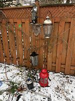 Full view of three garden lanterns, solar light, mounted fish planter, and fish statue mounted on wooden fence with snow-covered ground.