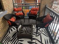 Set of four wicker armchairs surrounding a wicker coffee table frame without glass top on a black and white patterned outdoor rug.
