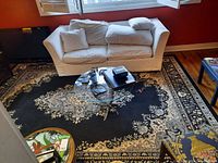 Living area with a white sofa on top of a large black area rug with cream floral patterns.
