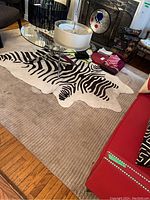 Faux zebra striped rug on top of a larger beige ribbed striped pile rug in living room setting with furniture around.