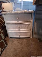 Front view of the white wicker side table showing the three drawers and cushioned top.