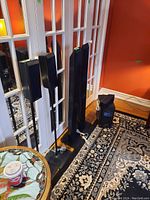 Four speakers and one subwoofer with cables in a room with orange walls and patterned rug