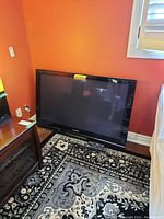 Full view of Panasonic television on carpet against orange wall next to furniture.