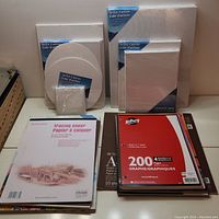 Variety of canvases stacked on left, spiral notebooks and paper pads stacked on right