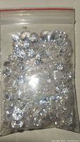 Resealable plastic bag filled with multiple clear, faceted faux diamonds of various sizes and shapes.
