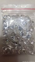 Small clear plastic resealable bag filled with clear faceted plastic faux diamonds in various shapes, round and teardrop.