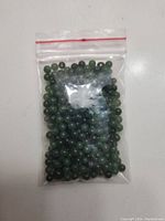 Plastic bag filled with small round green jade beads on white background, showing bead size and color.