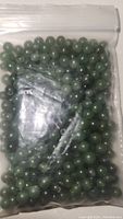 Sealed plastic bag filled with polished round jade beads, shown from one angle.