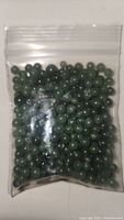 Plastic resealable bag filled with numerous small round green jade beads, showing color and quantity.