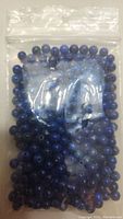 Plastic bag with dark and medium blue lapis lazuli beads, round shape, polished surface.