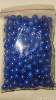 Clear plastic bag filled with deep blue round lapis lazuli beads spread densely inside.