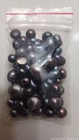 Plastic ziplock bag filled with loose black pearls of various sizes and irregular shapes.