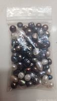 Front view of resealable plastic bag with varied loose pearls of different sizes and colors including black, white, and brown.