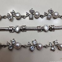 Close-up view showing two silver bracelets with faux pearls and clear rhinestones alongside a textured silver bracelet with rhinestone accents