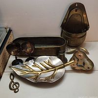 Photo showing entire brass lot including goblets, leaf tray, heart trivet, wall pockets, rectangular planter, and treble clef figure