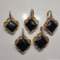 Five clip-on pendants with gold-tone metal, black square stones, and faux diamond accents arranged flat on a white surface.