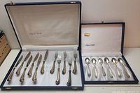 Full view of two cases containing the flatware set with knives, forks, and spoons arranged inside.
