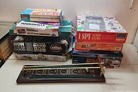 Stack of various boxed board games including I Spy Memory Game, Nabbit, Cranium, Powerballs, and others, with a wooden and brass game accessory in front.
