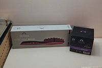 Full lot view showing SuTRA Ionic Heat Brush box and the Moroccan Hair Mask container side by side against a plain wall.