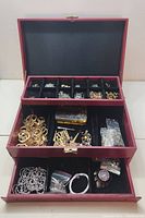 Full view of the red jewelry box open with three levels of compartments containing assorted jewelry findings and components.