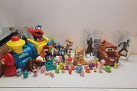 Photo of an assortment of kids toys including a Fisher-Price Little People Elmo train, various small figurines, and a Disney Pixar Cars Mater toy car.