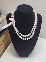 Front view of double strand faux pearl necklace displayed on black bust stand with brand and price tags attached