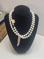 Front view of the faux pearl necklace displayed on a black bust stand, showing the full length and pearl arrangement with tag visible.