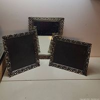 Set of one mirror and two picture frames with ornate silver-tone metal borders, displayed standing on a white surface against a plain background.
