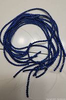 10 strands of tightly strung small round deep blue lapis lazuli beads, coiled loosely on a flat surface with visible clear threads.