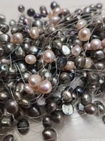 Close-up of mixed pearl strands showing white, pink, and black pearls on transparent threads.