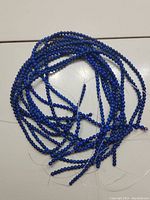 Photo showing the 10 strands of deep blue, round lapis lazuli beads loosely coiled together on a light surface.