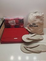Photo showing Corona branded cream fabric hammock bag, red travel organizer pack, and beige woven sandals.