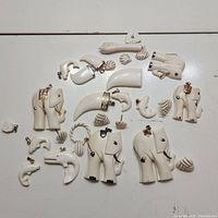 Top view of 18 white pendants arranged on a white surface, displaying various animal shapes including elephants, dolphins, a crocodile, a swan, and multiple small shell designs with gold-tone bails.