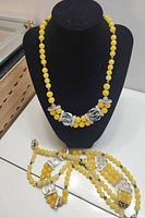 Three yellow gemstone bead necklaces shown on and next to a black bust display, highlighting yellow round beads and silver-tone embellishments