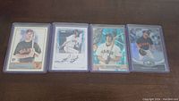Four Brandon Belt rookie baseball cards arranged side by side in protective sleeves on a brown surface, showing various designs including autograph and holographic effects.